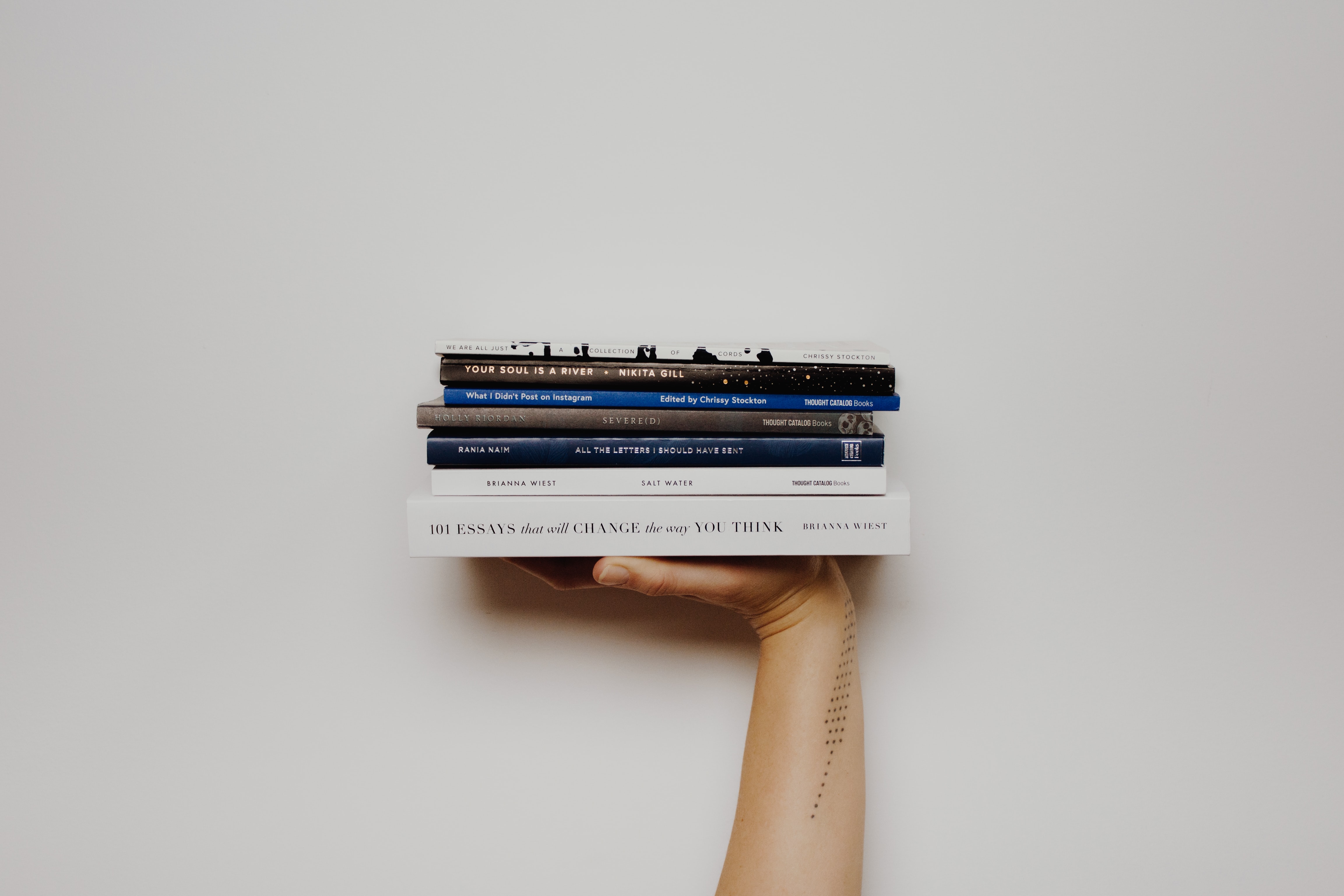 hand supporting six books horizontally on an offwwhite background