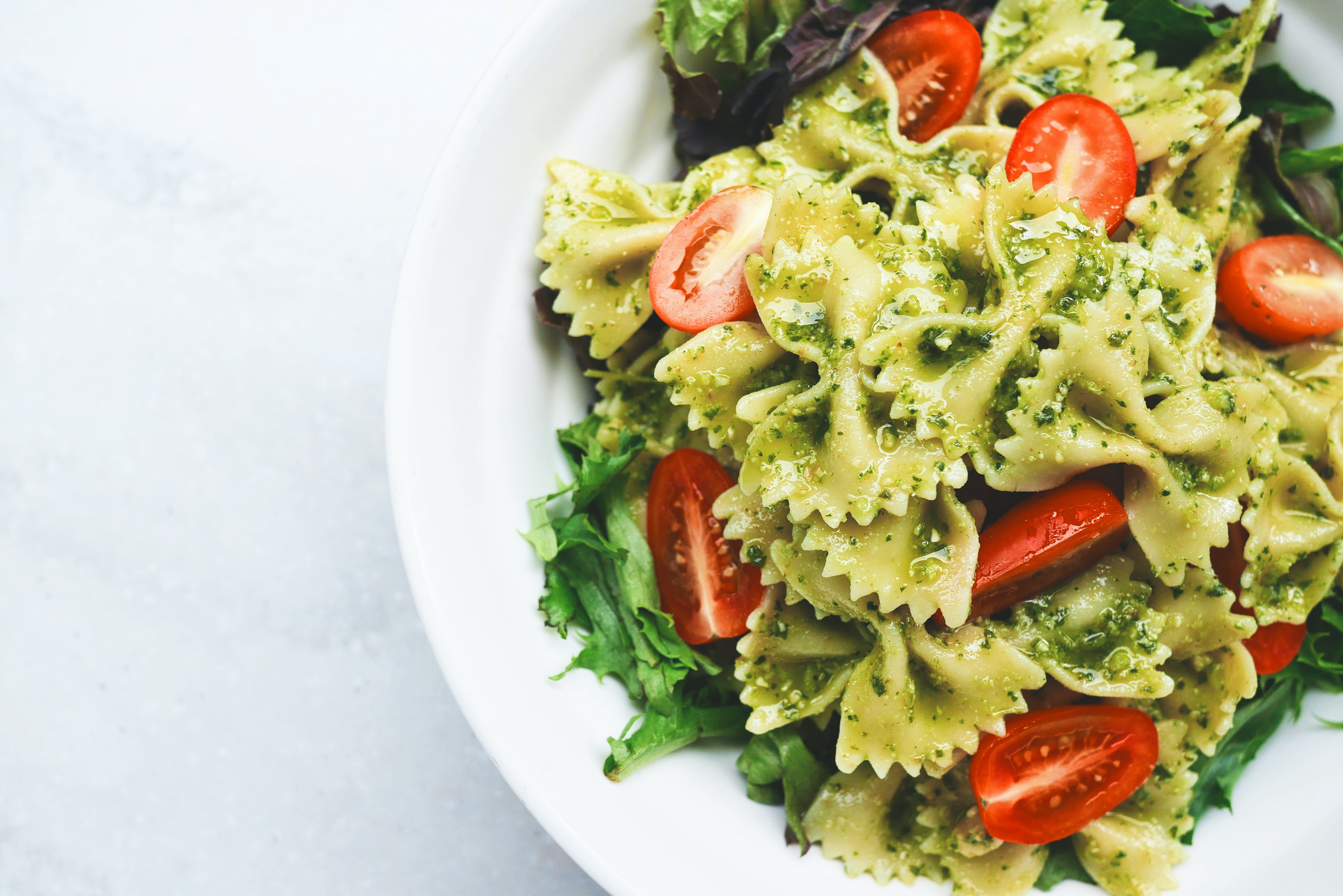 bowl of pesto pasta with tomato garnish on a white background